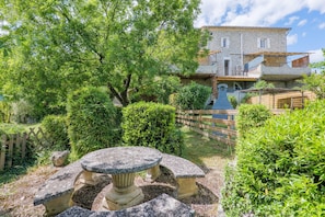 Un bâtiment en pierre avec un jardin, une clôture en bois et une table en pierre.