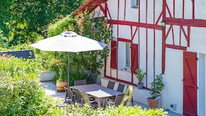 Een klassiek vakwerkhuis met een eetgedeelte, inclusief een tafel en stoelen, omgeven door potplanten en een grote parasol.
