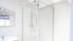 Een moderne badkamer met een douchecabine van glas, een wit wastafelmeubel en een spiegel met decoratieve lijst.