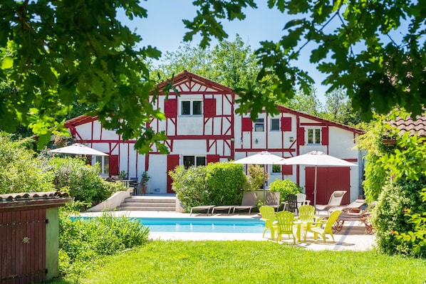 Un bâtiment à deux étages doté d’une piscine, d’un espace extérieur aménagé et d’une façade rouge et blanche.