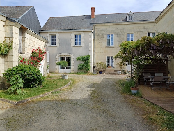 Une cour avec un chemin de gravier menant à un bâtiment aux murs de pierre et aux nombreuses fenêtres.