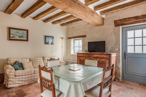 Une pièce avec un canapé à motifs à carreaux, une table à manger en bois avec des chaises, un téléviseur posé sur un meuble en bois et une porte avec une fenêtre.