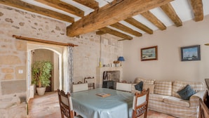 Una habitación rústica con vigas de madera a la vista, una pared de piedra, una mesa de comedor con sillas, un sofá y una planta en maceta.