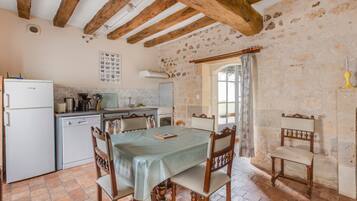 Une cuisine rustique avec des poutres apparentes, un dosseret carrelé et un coin repas comprenant une table et des chaises.