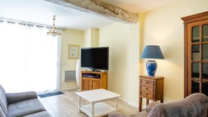 A living room with a sofa, a coffee table, a television on a wooden stand, a lamp, and a cabinet. - Gite de la Barthe – near Dax (Garrey)