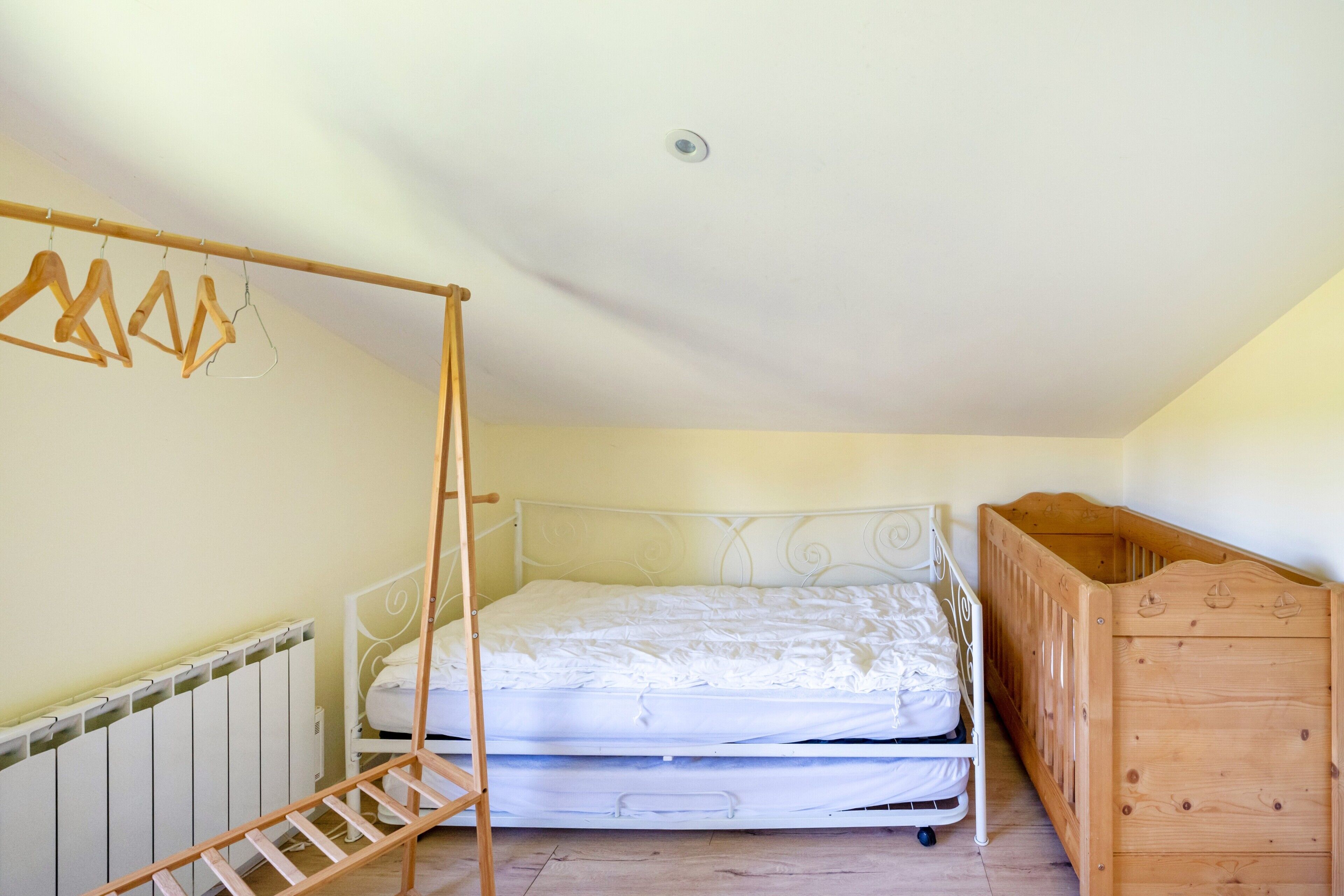 Una camera da letto con un letto, una culla in legno, un termosifone e un appendiabiti in legno.