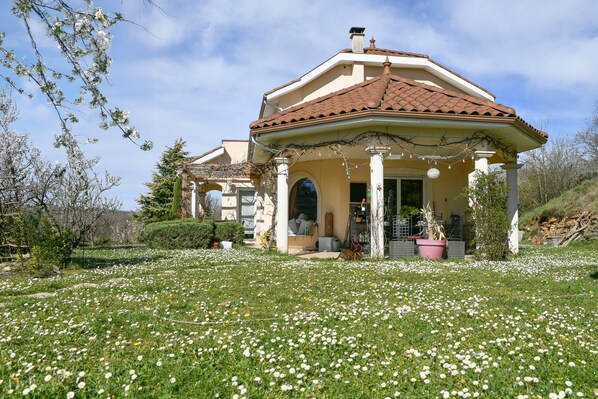 Una casa con porche cubierto, un jardín de flores blancas y un cielo despejado.