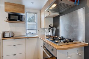 Une cuisine compacte équipée d’un four à micro-ondes, d’un grille-pain, d’une cuisinière et d’une fenêtre avec des stores.