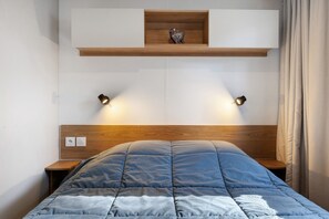 Une chambre à coucher avec une tête de lit en bois, une couvre-lit matelassée bleue, des lampes de chevet et une étagère ornée d’un objet décoratif.