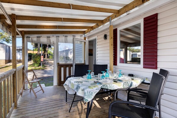 Une terrasse couverte avec une table dressée pour les repas, des chaises d’extérieur et une plateforme en bois.