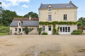 Un bâtiment en pierre de deux étages, avec une allée de gravier, une petite dépendance attenante et une véranda couverte.