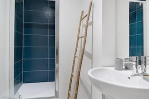 A bathroom with a white sink, a mirror, and a shower with blue tiles.