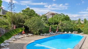 A swimming pool with lounge chairs and umbrellas, surrounded by greenery and a stone building in the background. - Gîte "Les Combes" with Shared Pool, Wi-Fi, and Air Conditioning (Chauzon)