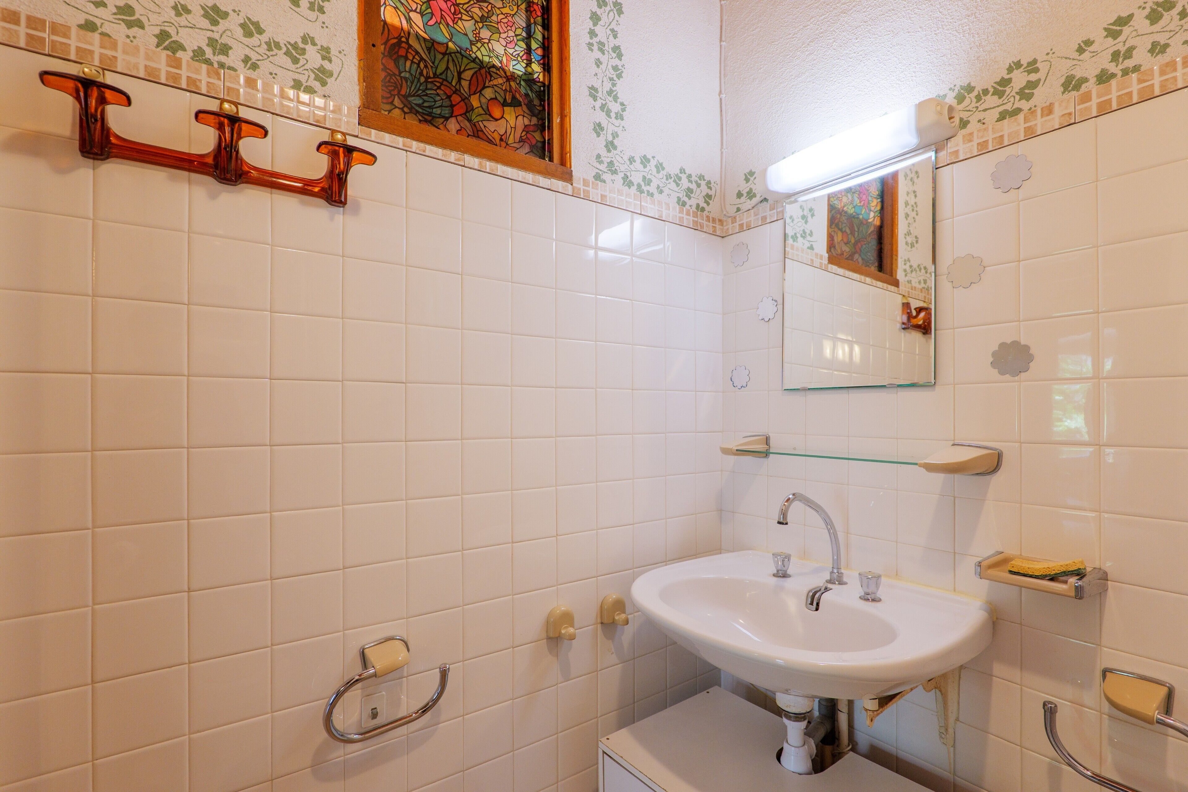 A bathroom with white tiles, a white sink, a mirror, and a towel rack.