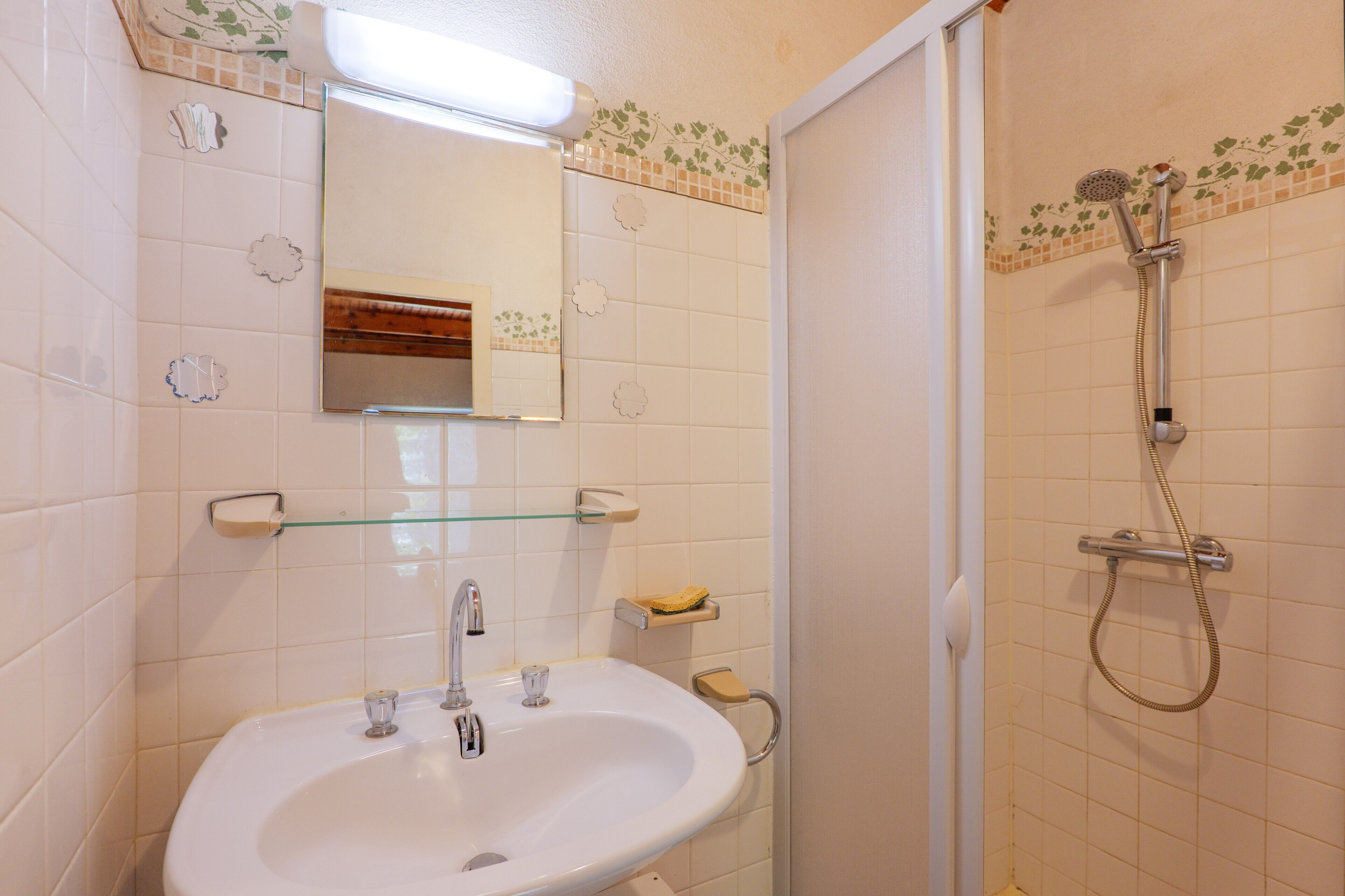 A bathroom with a sink, mirror, shower, and tiled walls.