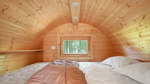 A cozy wooden cabin room with a bed, a window, and a ceiling light.