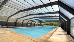 An indoor swimming pool with a glass ceiling, surrounded by a tiled floor.