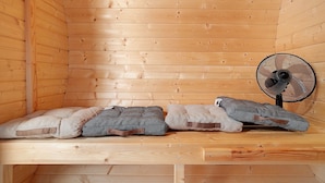 A wooden cabin interior with a bench, two cushions, and a fan.