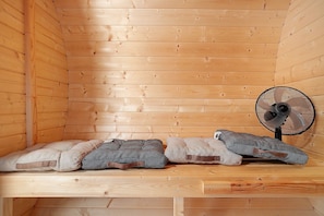 A wooden cabin interior with a bench, two cushions, and a fan.