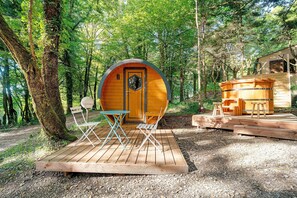 A wooden cabin with a circular door, surrounded by trees, and a small deck with folding chairs and a table. - Tiny Home La Sarladaise in the Forest with Sauna and Nordic Bath (optional) (Calviac-en-Périgord)