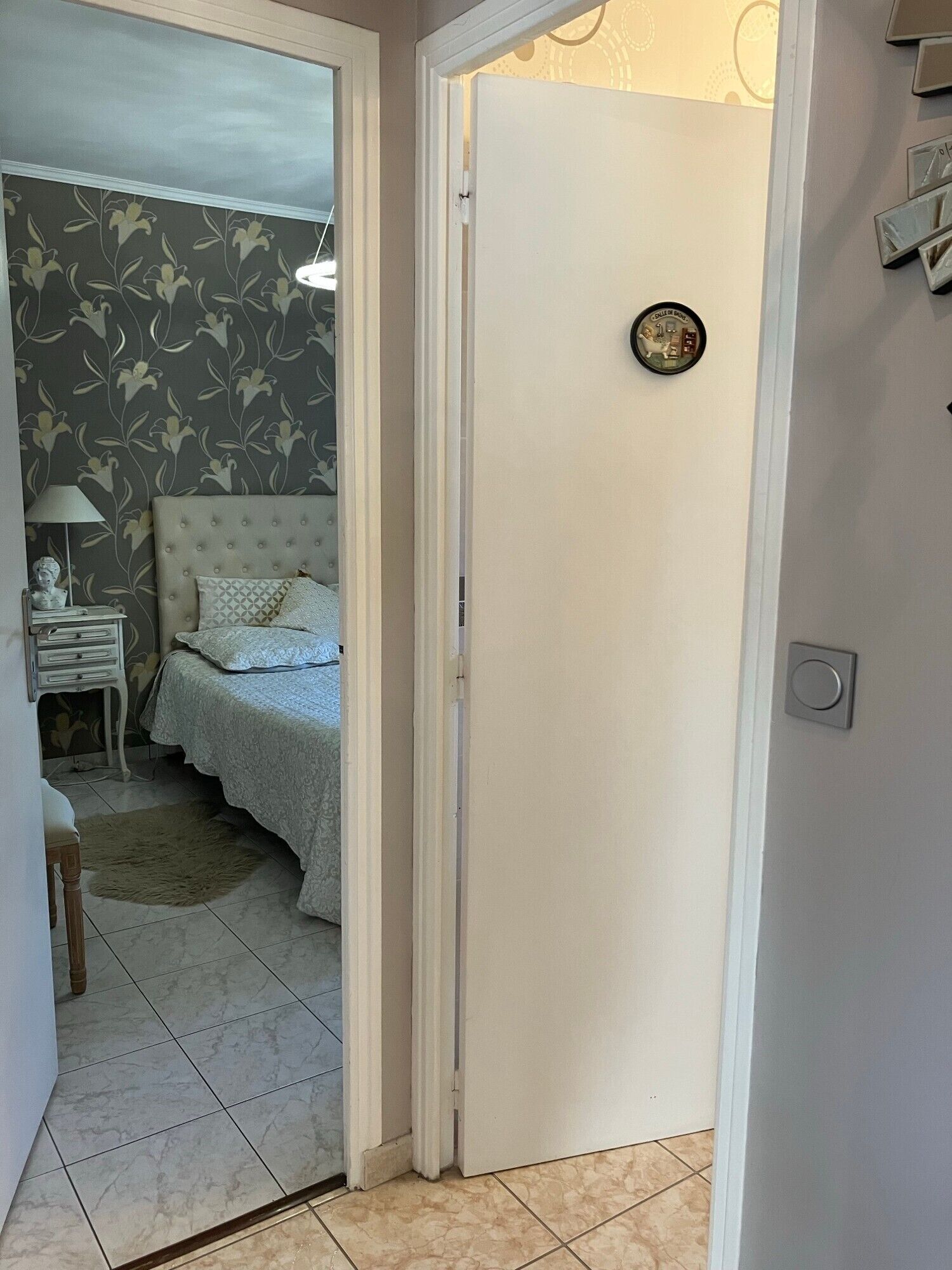 A bedroom with a bed, nightstand, lamp, and a door leading to another room.
