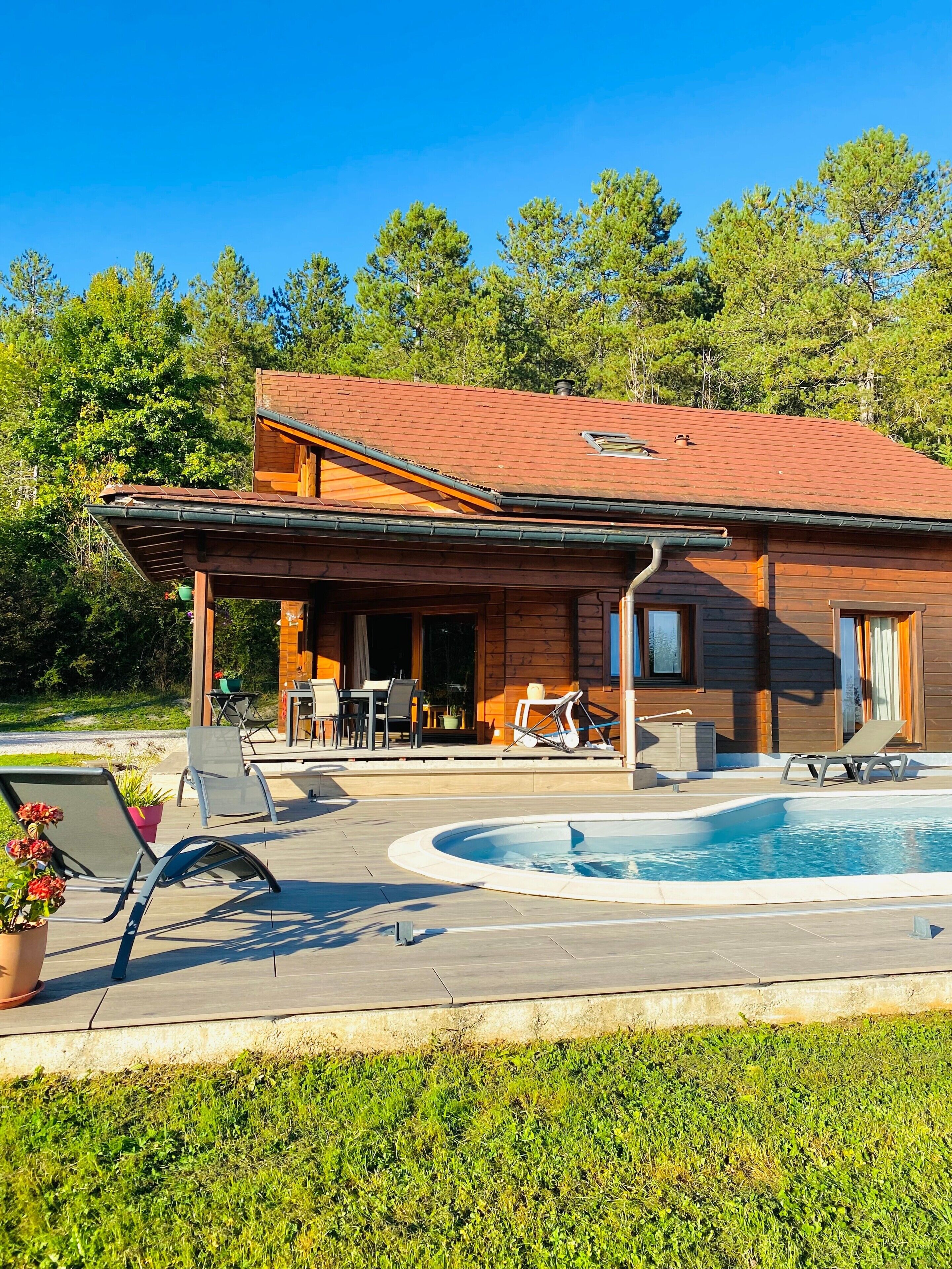 A wooden house with a covered patio, outdoor seating, and a swimming pool.
