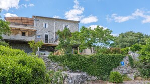 A stone building with a balcony, a parking sign, and lush greenery. - “Les Barlènes” Gîte with Shared Pool, Wi-Fi, and Air Conditioning (Chauzon)