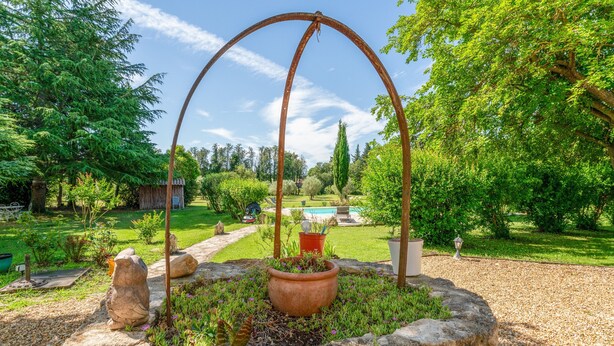 Un jardín con una estructura de piedra, un arco de metal y una planta en maceta.