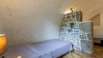 A small room with a bed, a stone wall, and a lamp.