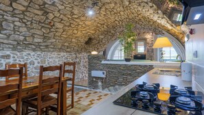 Un plafond en pierre, un îlot de cuisine avec une cuisinière à gaz, des chaises en bois et une table à manger.