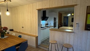 A modern kitchen with wooden cabinetry, a central island, and bar stools. - Gîte Les Pivoines with Private Terrace, Wi-Fi, and Air Conditioning (Saint-Robert)