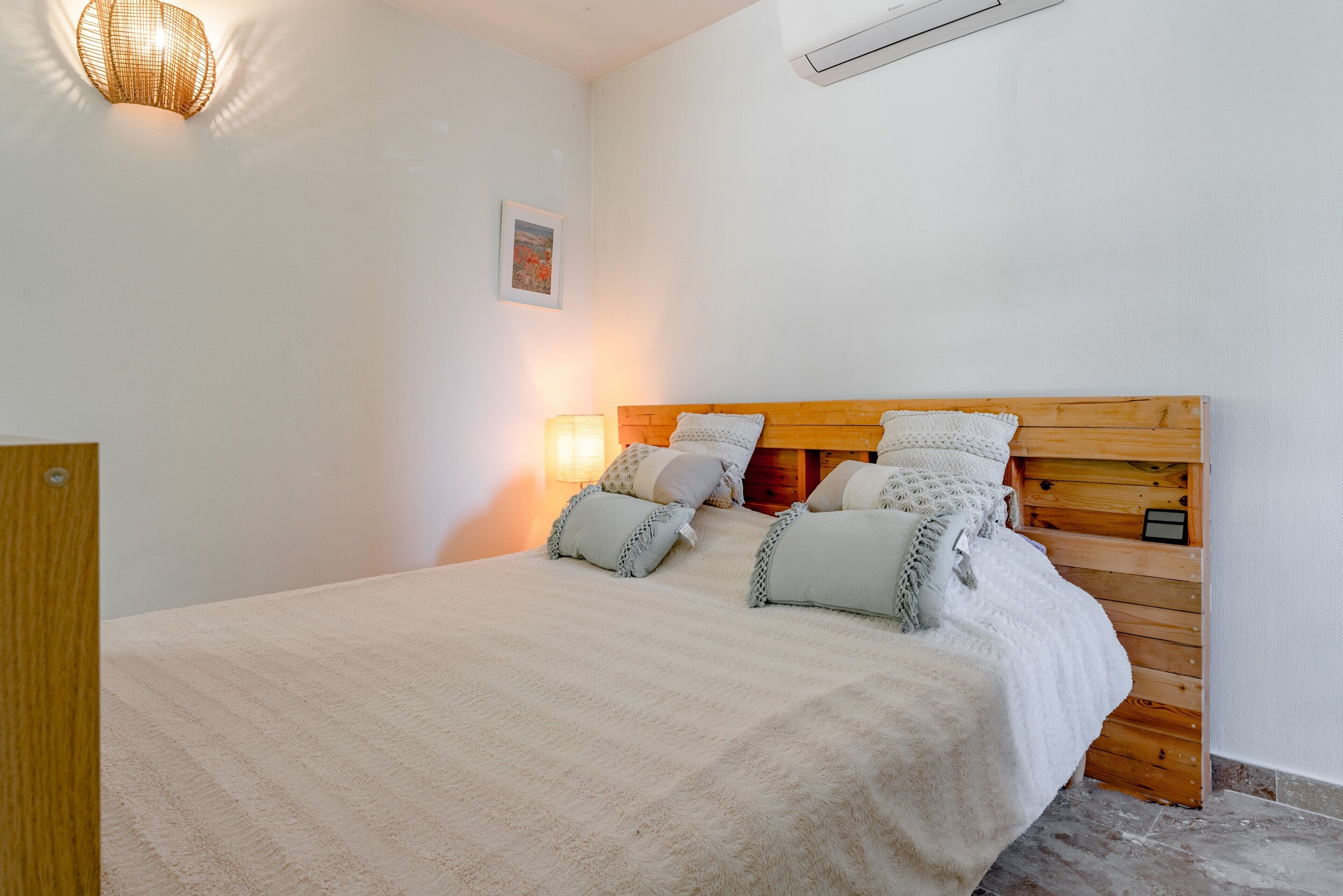 Una cama con cabecera de madera, una lámpara de noche y un aplique en la pared.