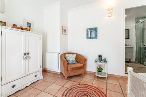 Une pièce avec un meuble blanc, un fauteuil marron, une petite étagère ornée d’objets décoratifs et un tapis à motifs.