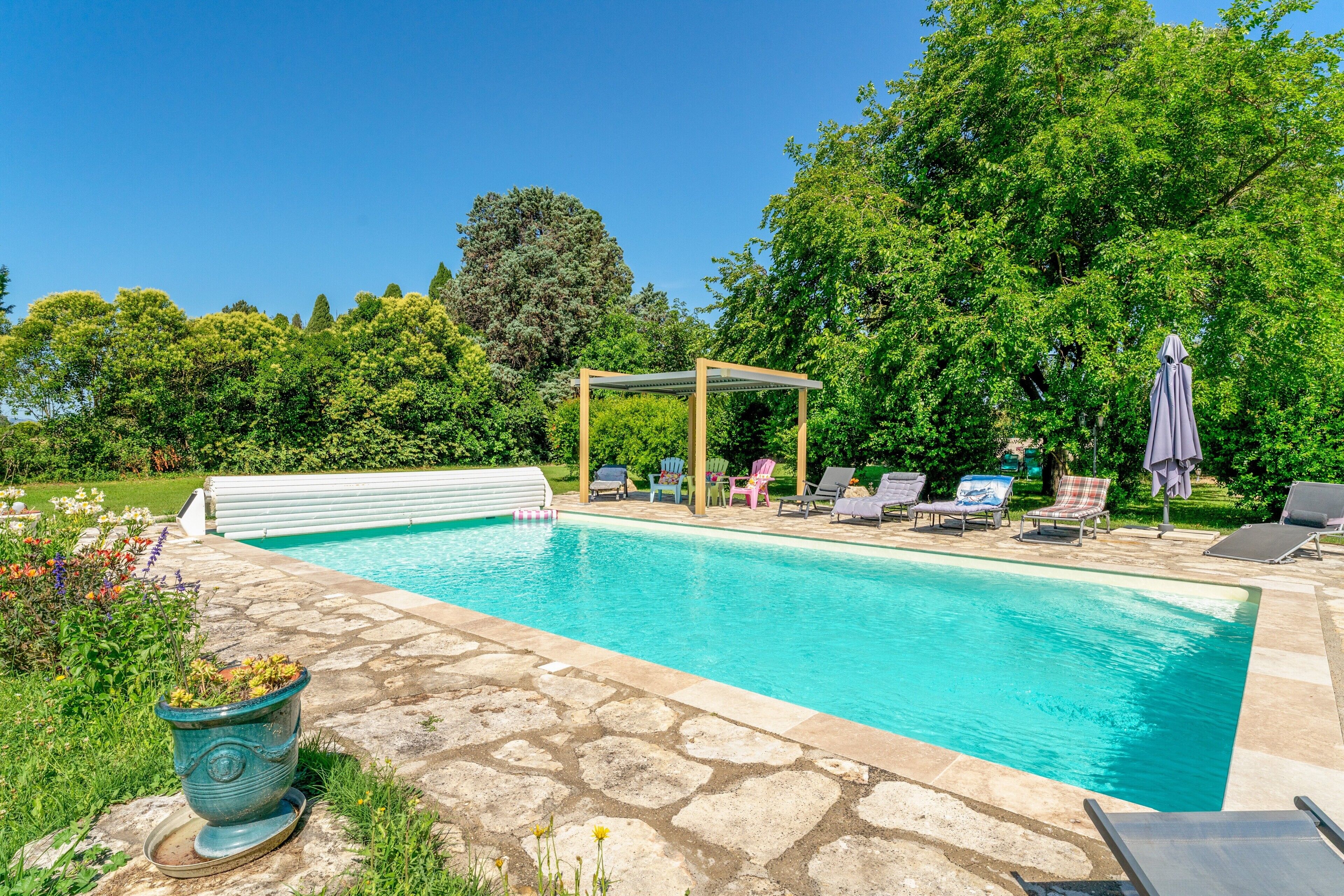 A swimming pool with lounge chairs, a pergola, and a stone patio.