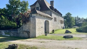 A stone building with a pitched roof, an arched doorway, and a small garden area with rocks and grass.