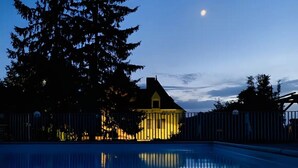 A swimming pool with a house in the background, surrounded by trees.