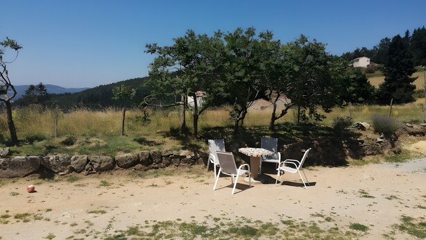 Una mesa y sillas en un entorno rural al aire libre, con cielo despejado y árboles al fondo.