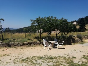 Ein Tisch und Stühle in ländlicher Umgebung, mit blauem Himmel und Bäumen im Hintergrund.