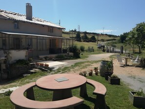 Ein Haus mit einer Terrasse, die einen runden Tisch und Stühle sowie Töpfe mit Pflanzen und einen Kiesweg zeigt.