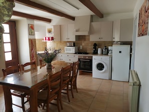 A kitchen with a dining table, chairs, a washing machine, a microwave, and a refrigerator.
