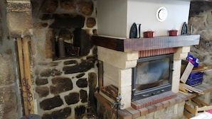 Una chimenea de piedra con un estufa de leña moderna, una olla metálica sobre la repisa y una base de ladrillo.