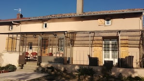 Un edificio de dos pisos con techo de tejas, chimenea y un área de estar exterior cubierta con sillas y mesas.