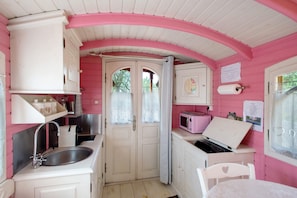 A compact kitchen with white cabinets, a sink, a microwave, and a small table. - Roulotte 'Au Bois Chéri' – Shared Pool and Wellness Facilities (Bussac Forêt)