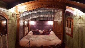 Una habitación con cama, paredes de madera, techo decorativo y ventana con cortinas.