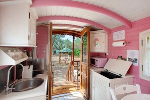A pink and white interior with a kitchen area, a dining table, and a view of the outdoors. - Roulotte 'Au Bois Chéri' – Shared Pool and Wellness Facilities (Bussac Forêt)
