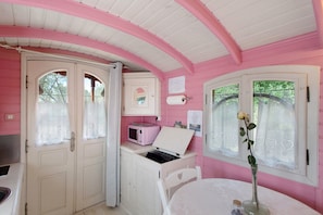 A pink-themed room with a white door, a microwave, a table with a vase, and a window with a rose. - Roulotte 'Au Bois Chéri' – Shared Pool and Wellness Facilities (Bussac Forêt)