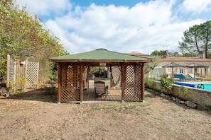 A wooden gazebo with a tiled roof, a pool, and a stone wall in the background. - Roulotte 'Au Bois Chéri' – Shared Pool and Wellness Facilities (Bussac Forêt)