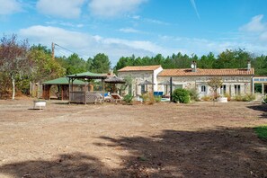 A rustic stone building with a tiled roof, surrounded by a fenced yard with a gazebo and lounge chairs. - Roulotte 'Au Bois Chéri' – Shared Pool and Wellness Facilities (Bussac Forêt)