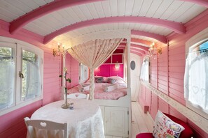 A pink-themed room with a canopy bed, a table with a vase, and a window with curtains. - Roulotte 'Au Bois Chéri' – Shared Pool and Wellness Facilities (Bussac Forêt)