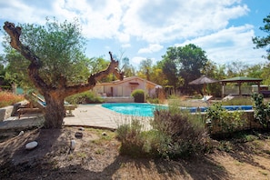 A pool area with a house in the background, surrounded by trees and a clear sky. - Roulotte 'Au Bois Chéri' – Shared Pool and Wellness Facilities (Bussac Forêt)